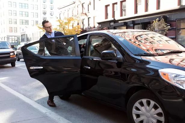 Young man, businessman getting into the back of a black car on a beautiful sunny day, door is open as he gets into the car with his briefcase, Commuting to work or going to the airport