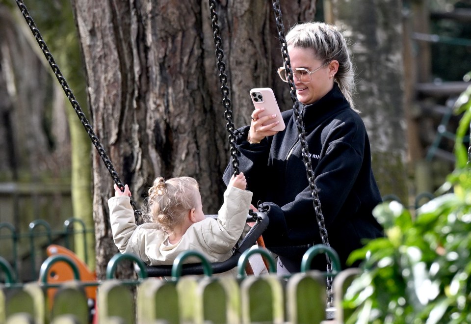 Woman taking a photo of her daughter on a swing.