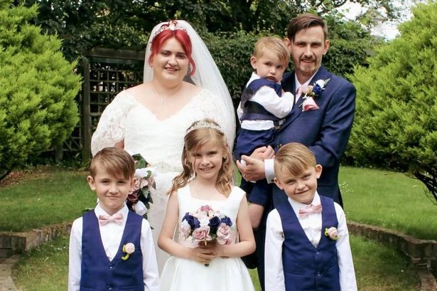 Photo of cancer patient Ashleigh Ellerton on her wedding day and pictured with her family. She is wearing a bridal dress and is standing next to her husband, wearing a blue tuxedo.