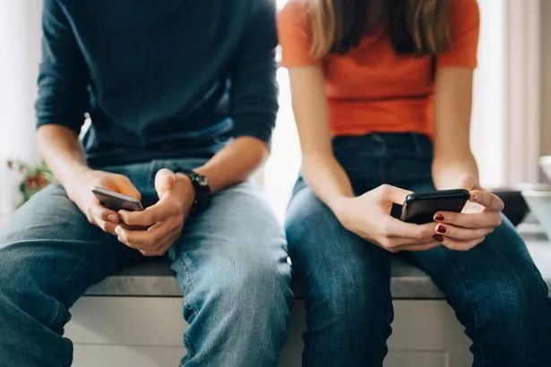 A picture of two people sitting down using their phones