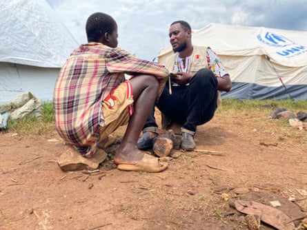 Emmanuel sits on a rock on the ground as he speaks with Dushime Entente Habib, who is crouched opposite