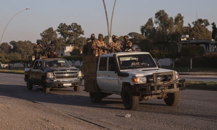 Syrian security forces conduct patrols in Latakia: two large pickup trucks are driven down a wide street with armed fighters standing in the rear flatbeds