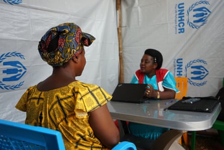 Therese sits at a table with her back to camera, facing the Save the Children worker