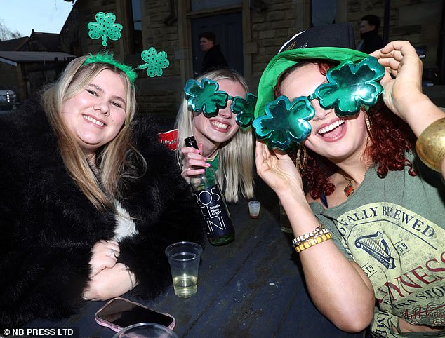 Three girls show off their oversized shamrock glasses while drinking at a bar in Leeds