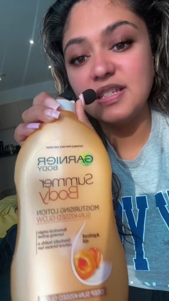 Woman holding up a bottle of Garnier Body Summer Body Sun-Kissed Glow Moisturizing Lotion.