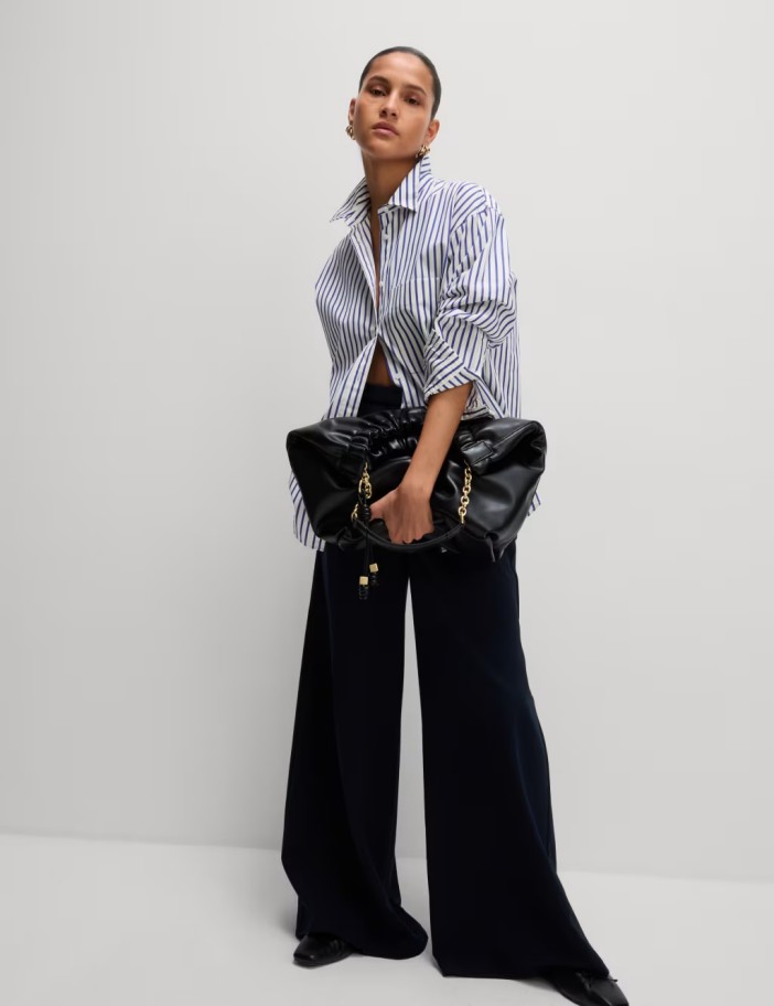 Woman in striped shirt and wide-leg pants holding a black bag.