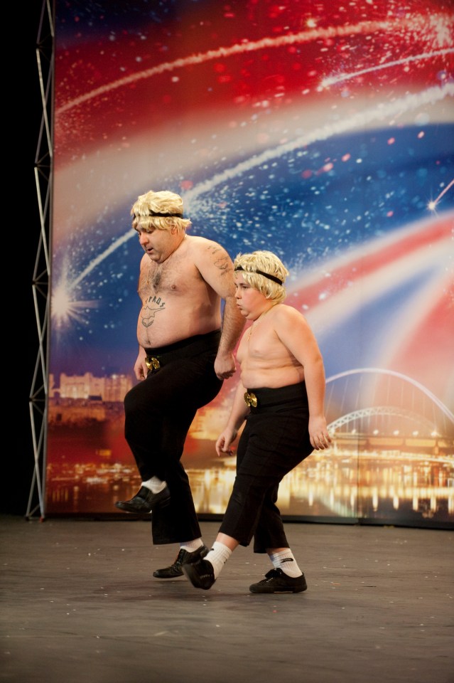 Two shirtless men in black pants and white socks performing on a Britain's Got Talent stage.