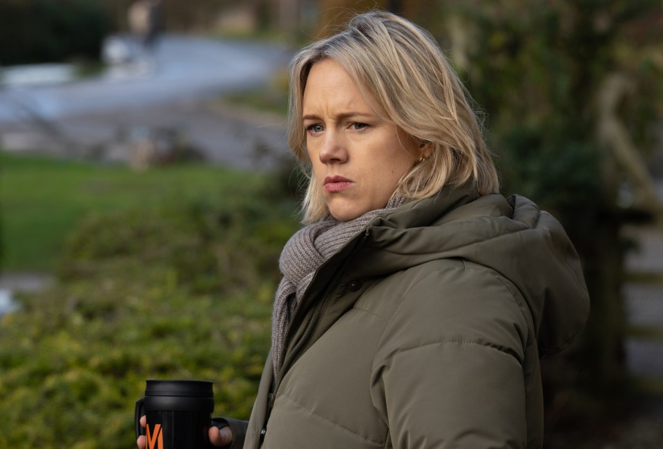 A woman in a puffer jacket looks thoughtfully off to the side, holding a travel mug.