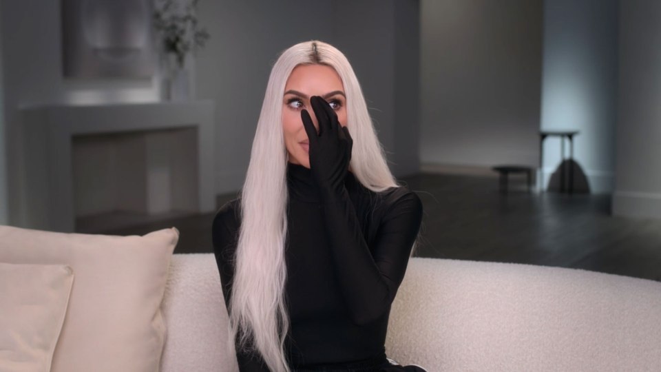 Kim Kardashian crying on a couch, covering her face with her hand.