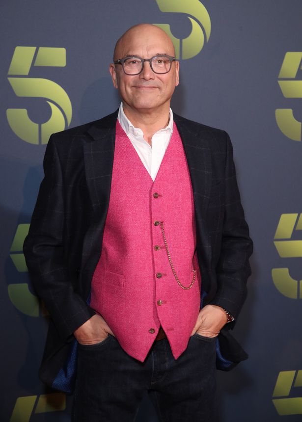 Gregg Wallace in a white shirt, pink waistcoat, black jacket and dark trousers.