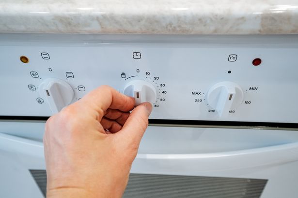 A person is cautiously adjusting a knob on a white oven