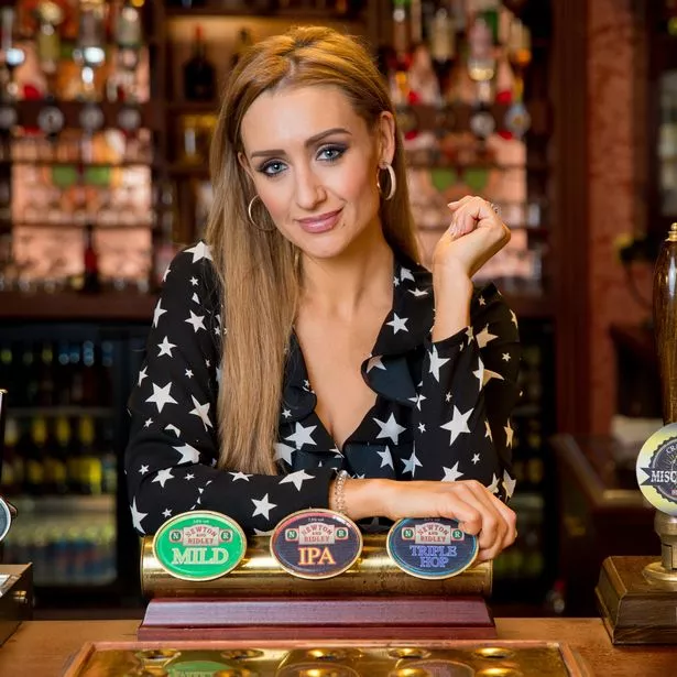 Catherine Tyldesley, in a black top with white stars on, stood behind a bar on the set of Coronation Street.
