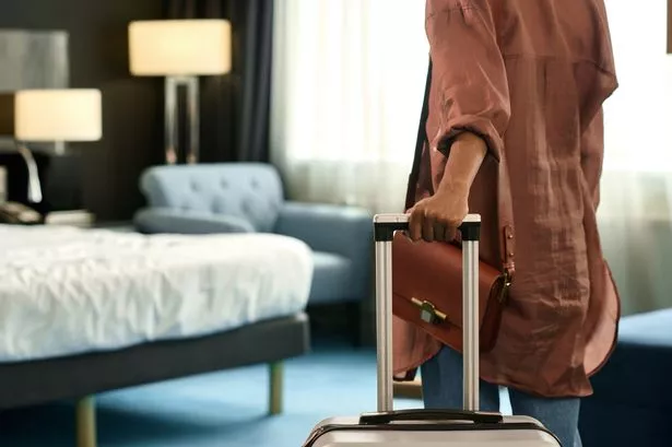 Close up of unrecognizable Black woman entering hotel room and holding suitcase upon travelling to resort copy space