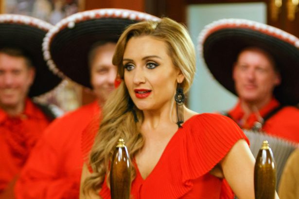 Catherine Tyldesley, in a red dress, stood in front of the bar on the set of Coronation Street.