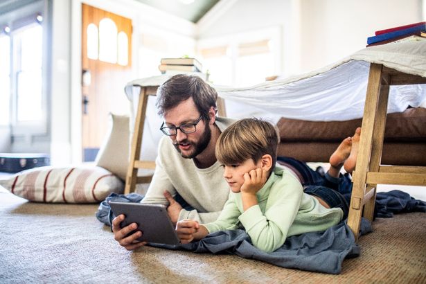 Father and son watching digital tablet in homemade fort