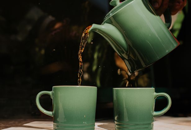 Two green cups sit outside. Tea is poured into the mugs from a matching tea pot.