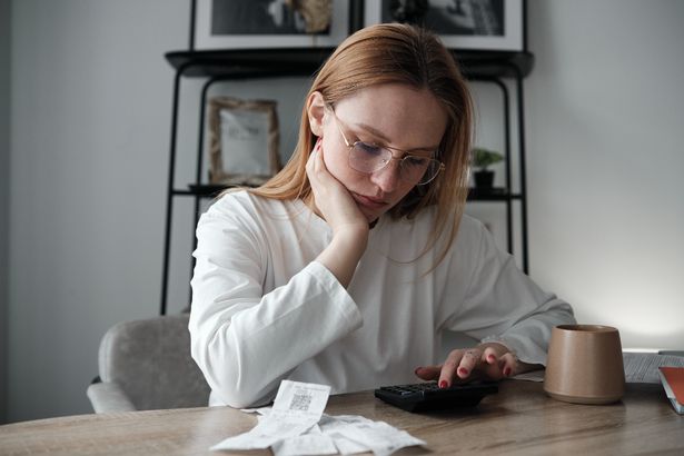 Young woman calculating spendings looking at bills using calculator while sitting at table. Monthly expenses