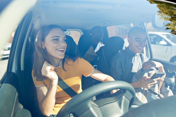 Happy young woman dancing with friends seen through car windshield on sunny day