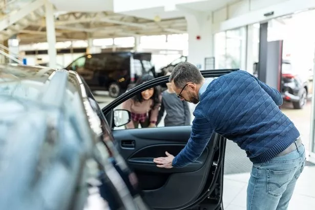 Mature man checking the new car door while his wife and son standing by at the dealership. Family choosing automobile with son in showroom.