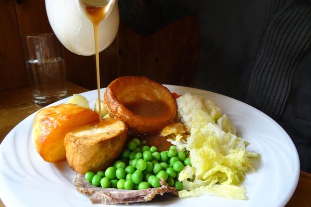Photo showing a traditional Sunday roast dinner served up on a round white plate with a selection of seasonal vegetables, pouring gravy from a china gravy boat jug.