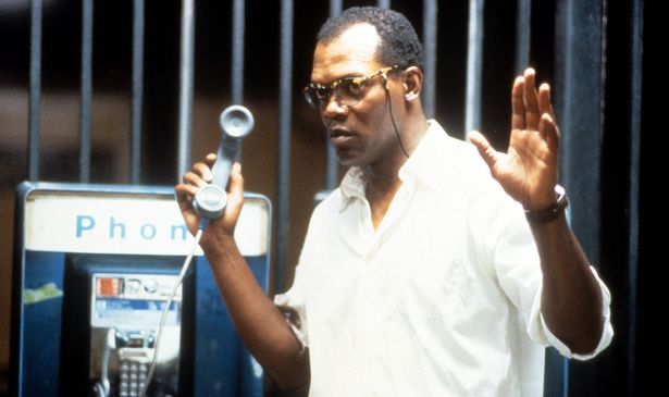 A man in glasses holds a phone and his hands in the air