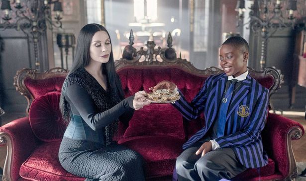A woman offers a girl a plate of food as they sit on a couch