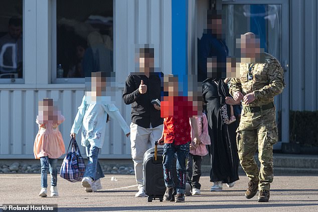 A soldier escorts a family at Stansted on May 23 as part of a government scheme costed at £7billion smuggling migrants to Britain after a data-leak blunder exposed by the Daily Mail