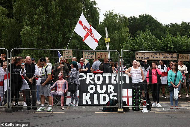 Protesters stand behind a fence as they gather near the Bell Hotel during a protest against the use of the hotel as migrant accommodation on July 27, 2025 in Epping