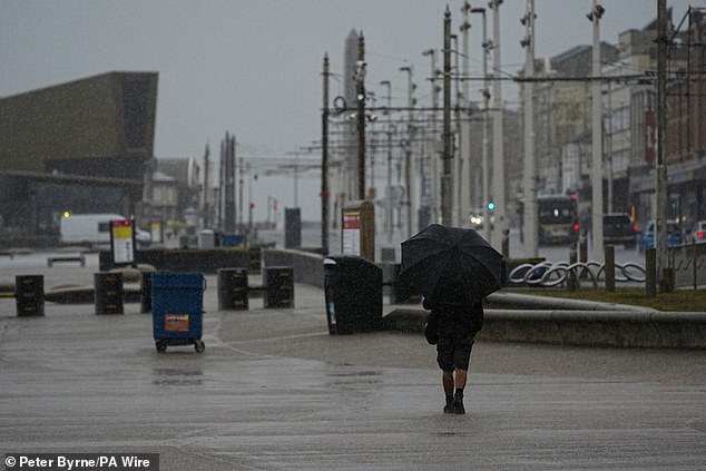 A man takes shelter from the wet weather beneath an umbrella as he walks along the promenade in Blackpool