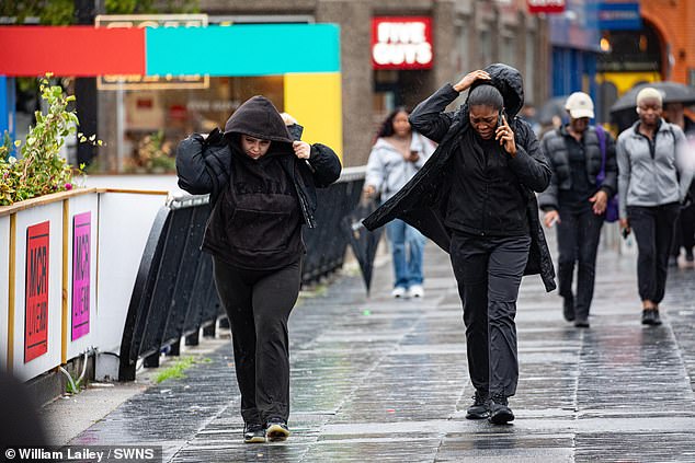 Two people battle the wind and rain in Manchester as one tries to make a phone call during the storm