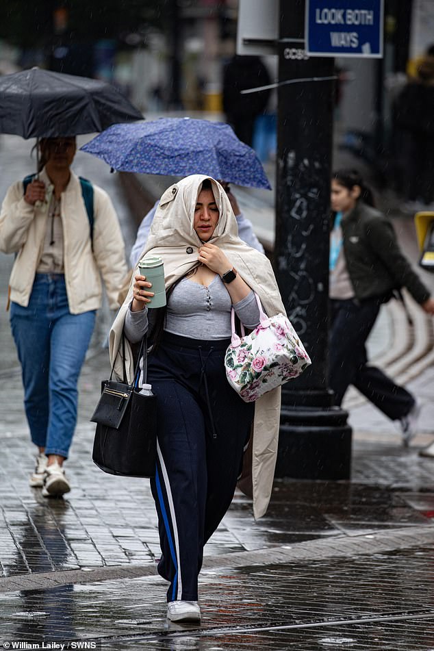 A woman holds her coat over her head as she travels through Manchester City Centre this morning