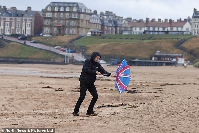 a man struggles with his umbrella in the strong winds on Tynemouth Longsands beach