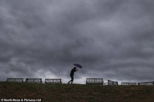 A man holding a union flag umbrella walks underneath dark storm clouds at Tynemouth