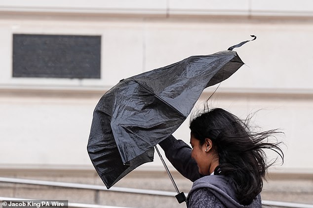 A woman struggles with their umbrella during windy conditions in Birmingham
