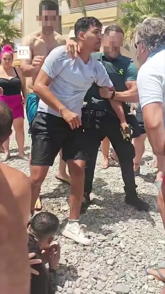 Bathers and members of the Spanish Civil Guard are seen holding back the disembarked migrants on Sotillo Beach