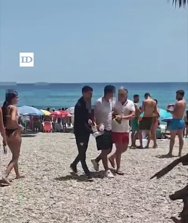 A man believed to be a migrant is seen being escorted by beachgoers
