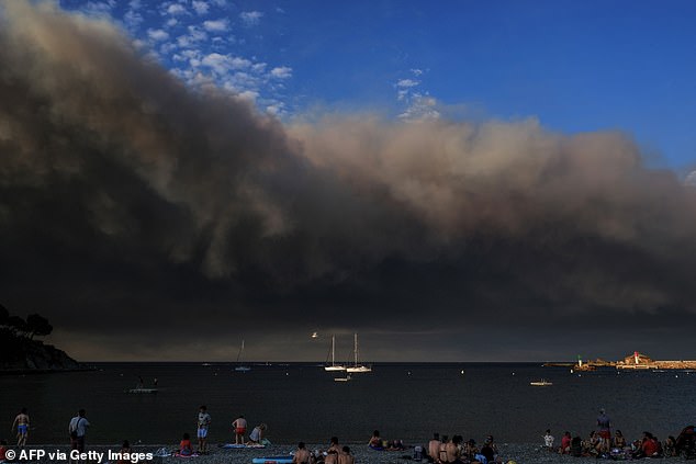 Tourists sit on the beach as the smoke from wildfires raging in the Aude department is seen from the Mediterranean coast in Banyuls-sur-Mer, southwestern France, on August 5