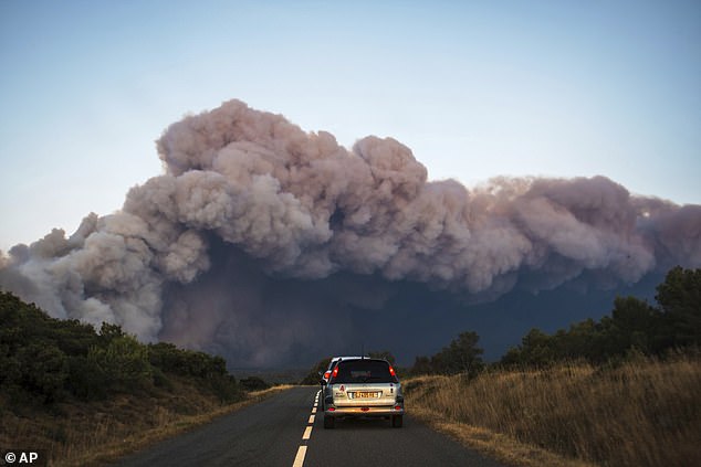 Cars drive past a fast-moving wildfire in a Mediterranean region of France near the Spanish border