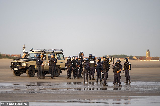 French riot police stand on the beach as migrants board small boats off the coast of France