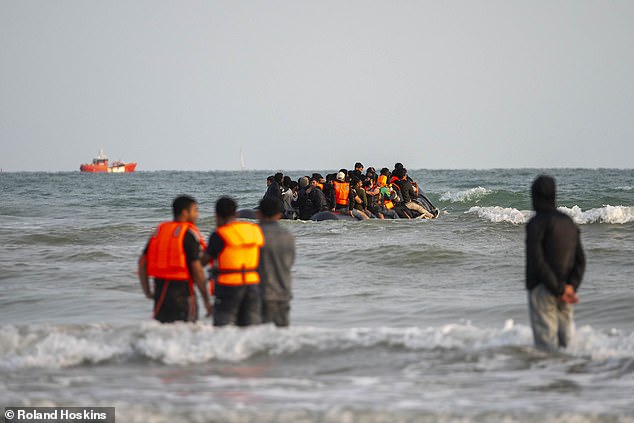 Migrants wait in the sea to be picked up by a dinghy to cross the English Channel as others are seen onboard the rubber vessel