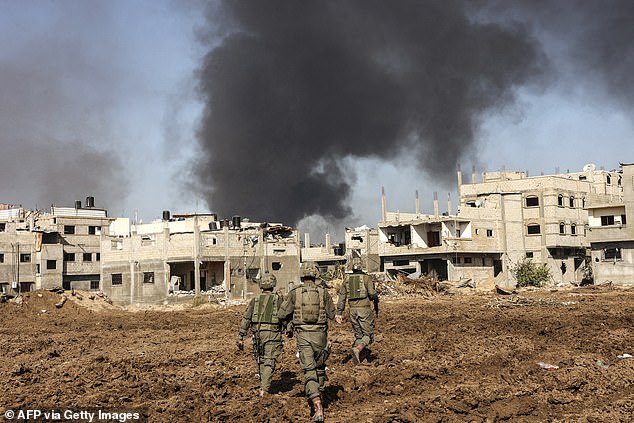 Israeli soldiers walking next to damaged buildings as smoke billows during a military operation in the north of the Gaza Strip amid continuing battles between Israel and the Palestinian militant group Hamas