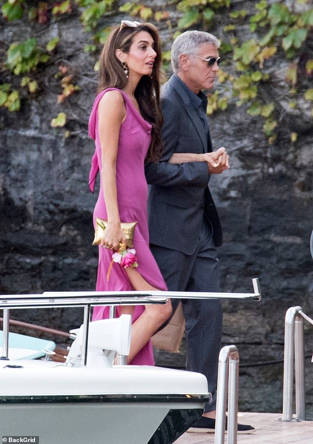 Amal exuded elegance in a flowing fuchsia gown with a high slit and bow detail, paired with a gold clutch and pink bouquet