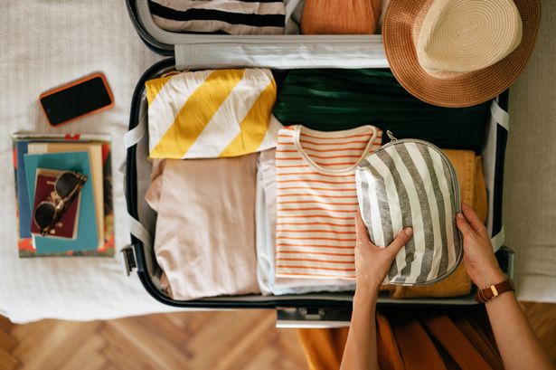 Shot from above of an anonymous woman packing things in her suitcase on the bed.