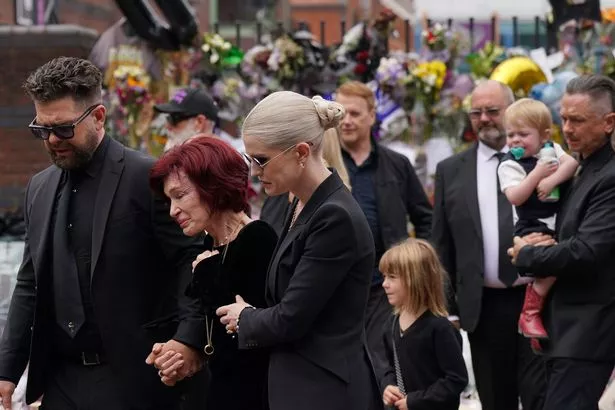 The family of Ozzy Osbourne, Jack and Kelly Osbourne, embrace as they view the messages and floral tributes left at th