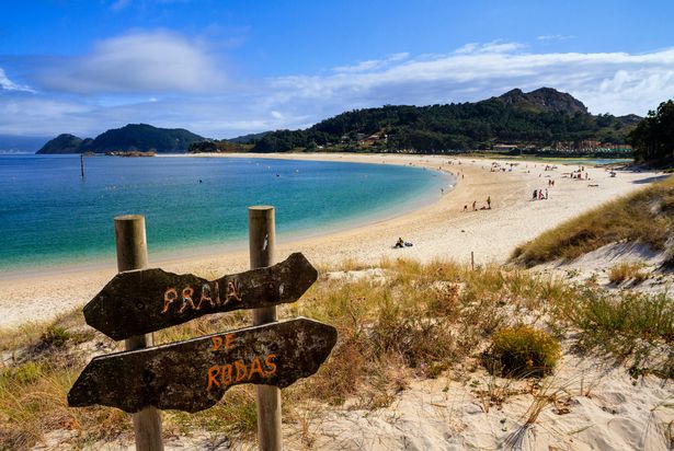 Image of the sign for Rodas beach with the beach landscape and water in the background