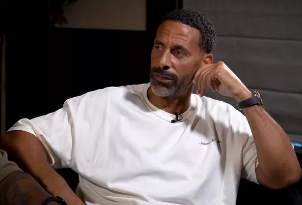 Rio Ferdinand wearing a white shirt and sitting on a chair, speaks to the camera while leaning on his arm