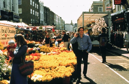 Hugh Grant walks along road by market stalls