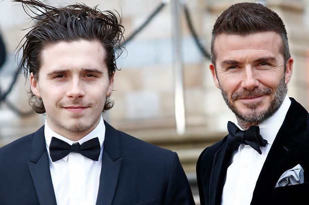 Brooklyn Beckham and David Beckham in black suits.