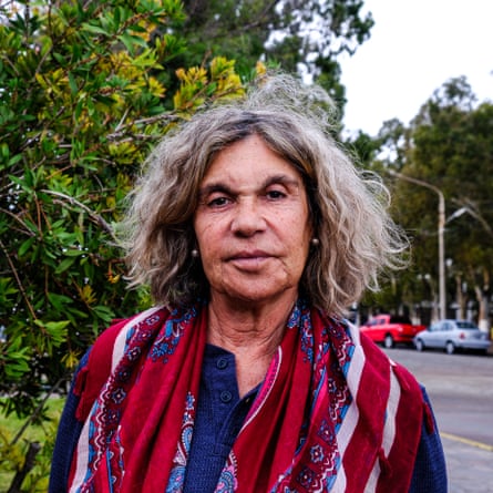 An older woman with a weather-beaten face poses by a road
