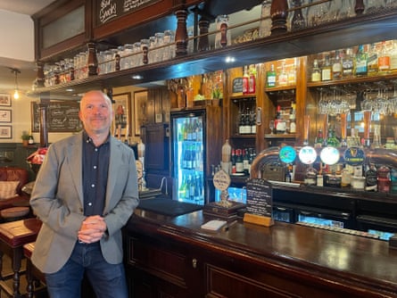 Jonathan Lawson leans on the bar at the Punch Bowl pub in Mayfair, London; he has a short grey beard and wears a grey jacket and blue jeans